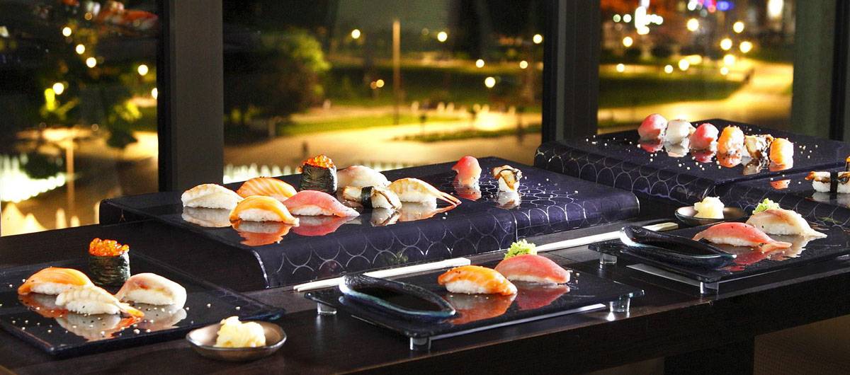 Beautiful sushi tableware in dark blue with night cityscape on the background.