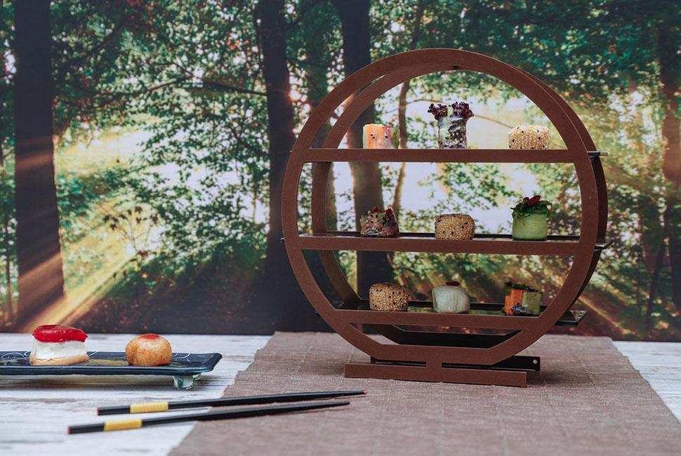 Tea tray Nata is a round tiered high tea stand with three tiers. Nata stands on a sunny forest background and is presenting beautiful Japanese desserts.