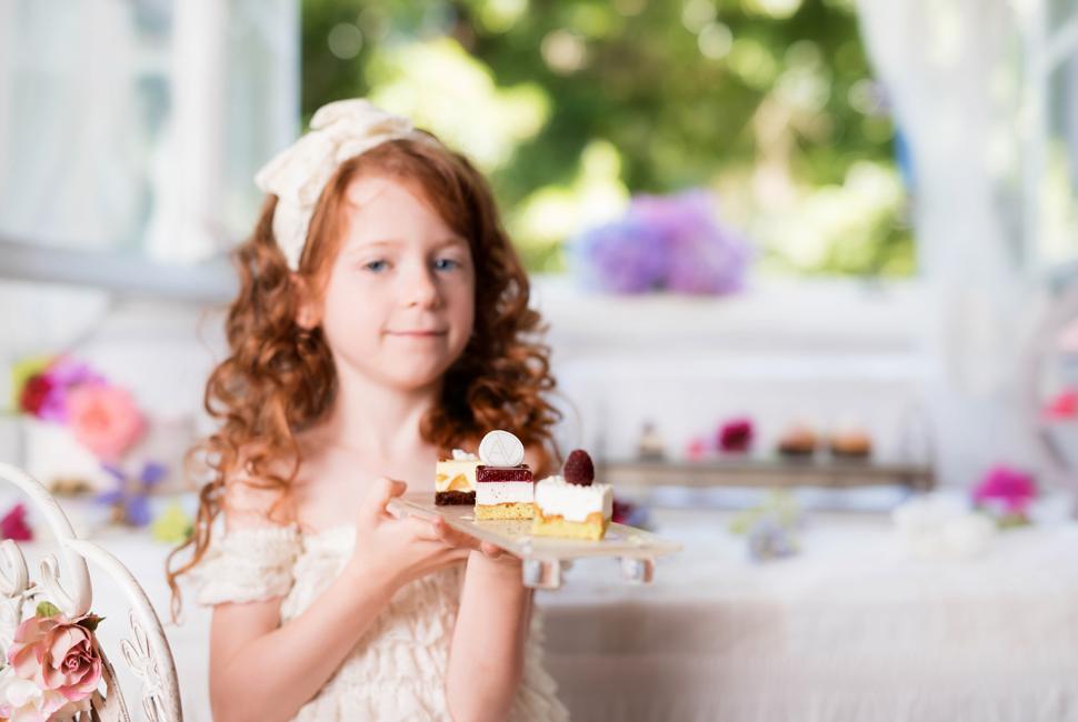 Ginger head little girl behind a lovely afternoon high tea stand Deu with small delicious dessert bites. tea stand with four levels. Each level is in a champagne colour decorated with our Sixties pattern.