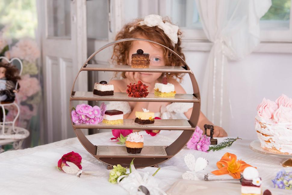 Ginger head little girl behind a lovely afternoon high tea stand Deu with small delicious dessert bites. tea stand with four levels. Each level is in a champagne colour decorated with our Sixties pattern.