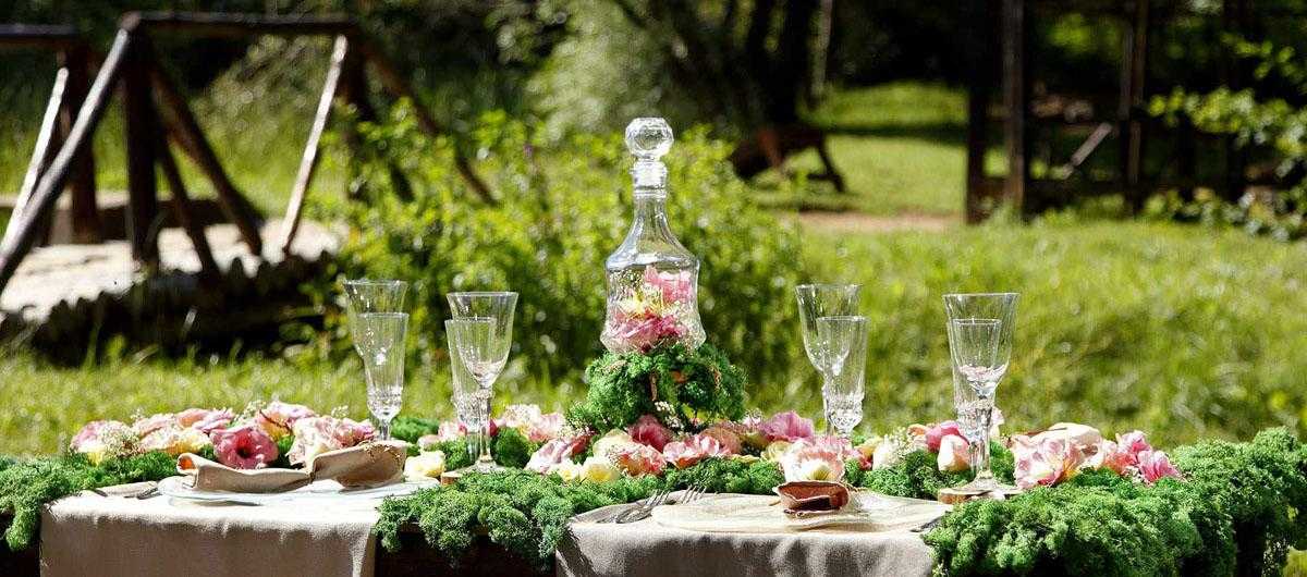 A fary like table setting in a very green environment outdoors. Flowers, forest feeling with glass plates and glasses.