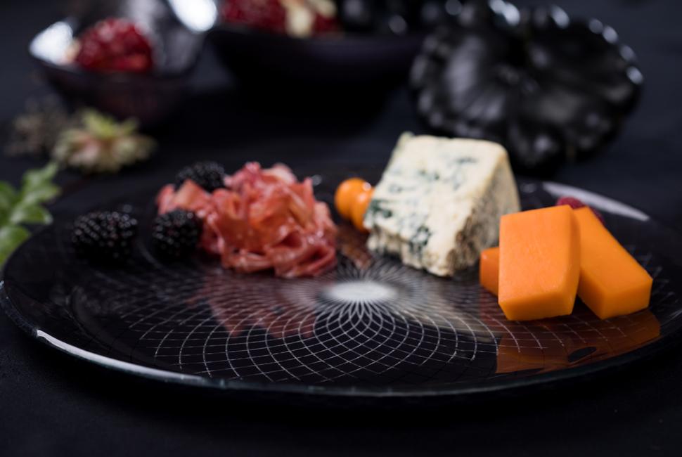 Kate is a big round dinner plate with a gently raised rim, in magical deep night blue with our lattice Venetian Filigree pattern. On the image Kate is presenting as a finger food platter cheese and meat bites as part of an environment of a Halloween tablesetting.