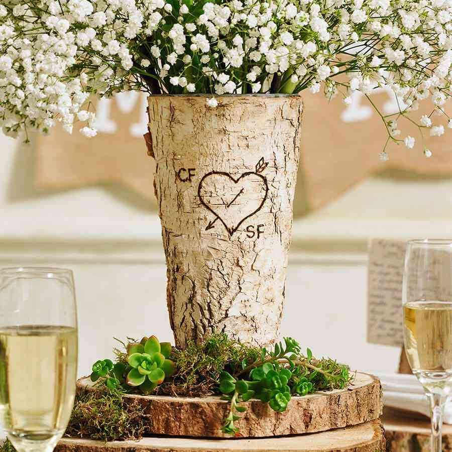 Fairy like environment table setting with a vase made from real tree and a heart carved on it with white flowers. On the table are also glasses of wine