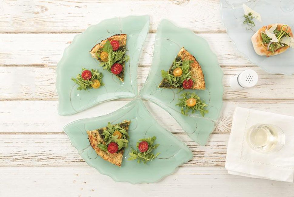 Pizza plate Dora is a lovely fan-shaped tapas plate in jade green with our alluring Vivace pattern. Dora is presenting lovely pizza with cauliflower crust and cherry tomatoes. Dora is positioned on white wood background.