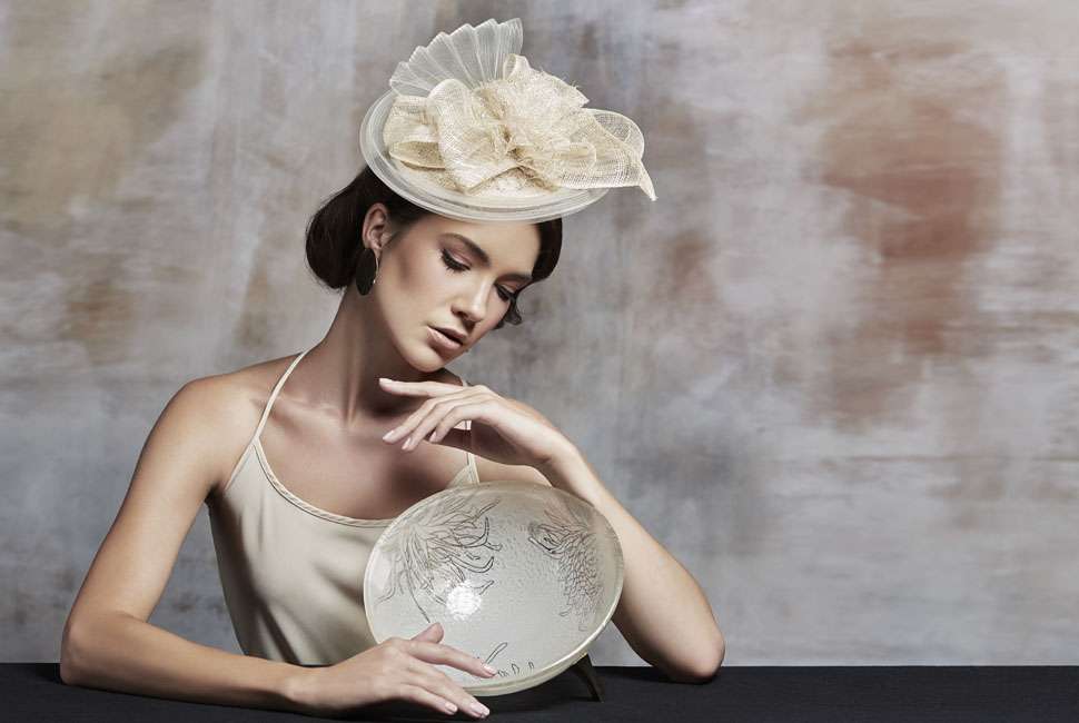 Beautiful lady dressed in the style of the Spring racing events in Melbourne Australia is presenting Marc is a medium sized fruit bowl in a tender cream colour decorated with our playful Perky Chrysanthemum design sitting on shiny hand crafted bronze supports