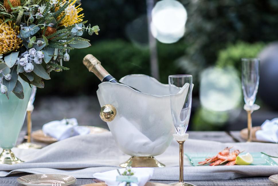 Table Setting Sharmi is a lovely cream glass ice bucket for champagne or wine. It stands on a handcasted and hand polished bronze pedestal and has two shiny bronze handles.
