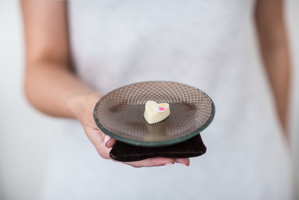 Woman's hands holding petit fours plate on a pillow with small heartshaped dessert in it