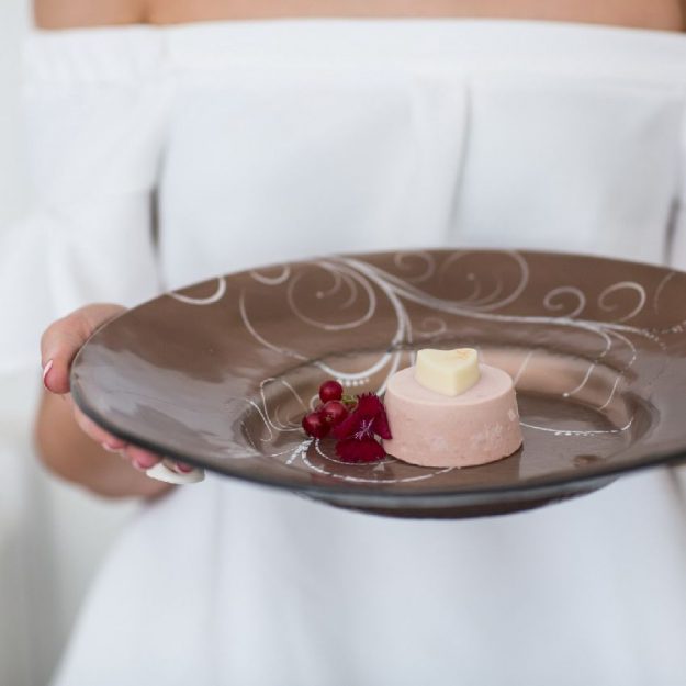 Large brown dessert plate held by hands with dessert